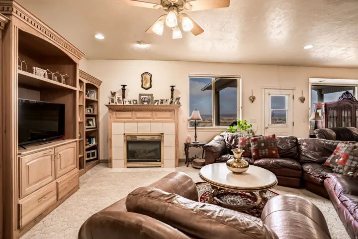 Living area featuring a fireplace with a tiled surround and wood mantel, built-in shelving with cabinetry, a ceiling fan with integrated lighting, and recessed lighting