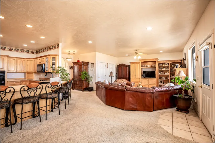 Open-concept living area featuring a kitchen island with bar seating, light wood cabinetry, recessed lighting, and a built-in entertainment center