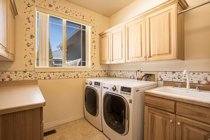 Functional utility room featuring a large window, ample wood cabinetry, an integrated sink with a countertop, and durable tile flooring