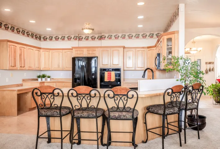 Spacious kitchen featuring light wood cabinetry, a built-in oven, black refrigerator, and a breakfast bar with seating