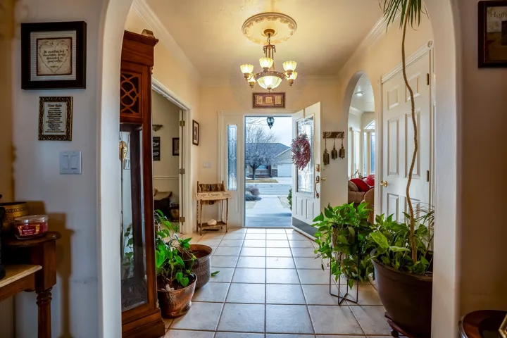 Foyer featuring neutral tile flooring, arched doorways, a decorative chandelier with a ceiling medallion, a white panel door, and an entryway with a glass-paned door