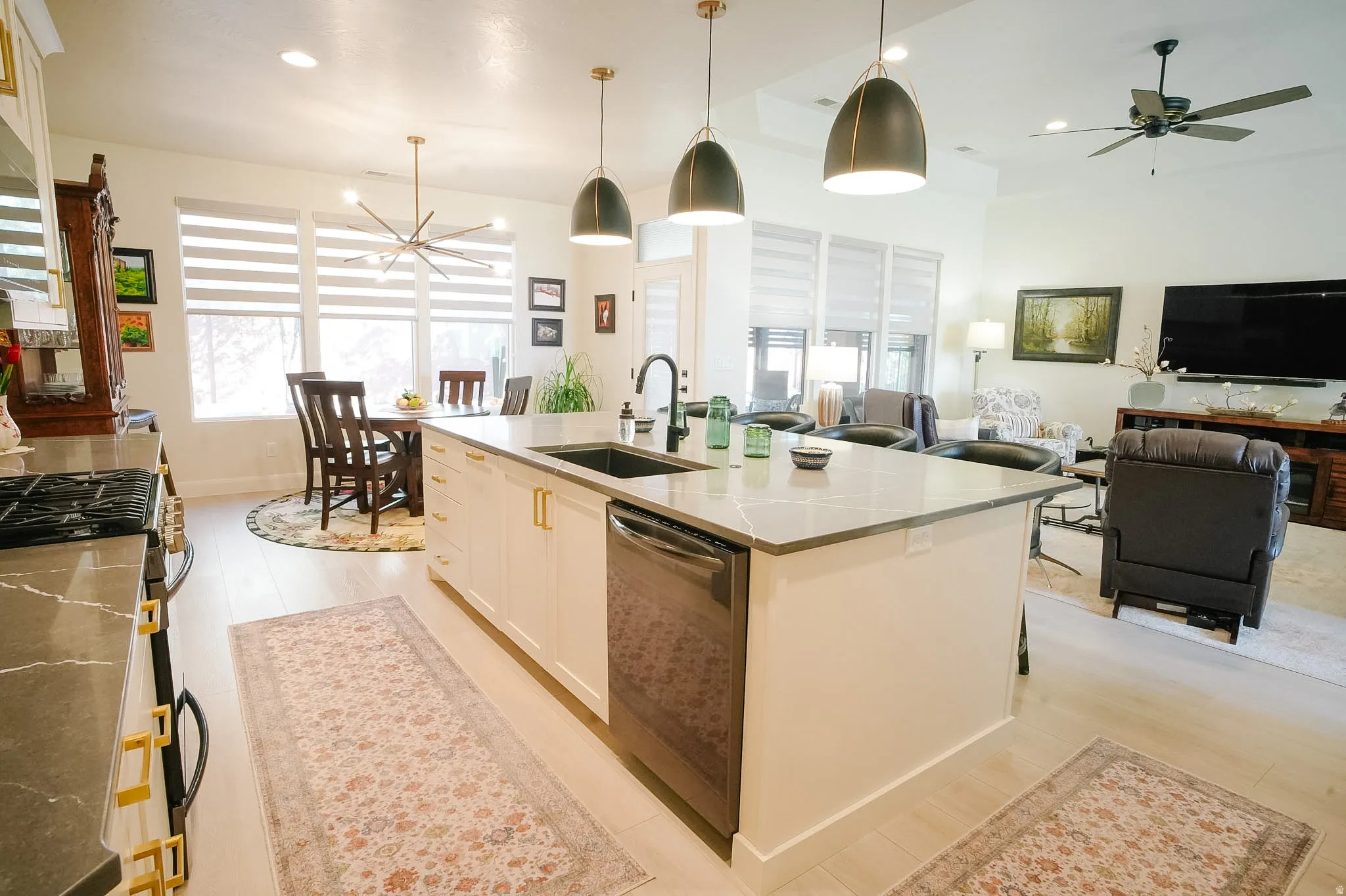Open-concept living area featuring a kitchen island with stone countertops and a built-in sink, light wood-finish flooring, and recessed lighting