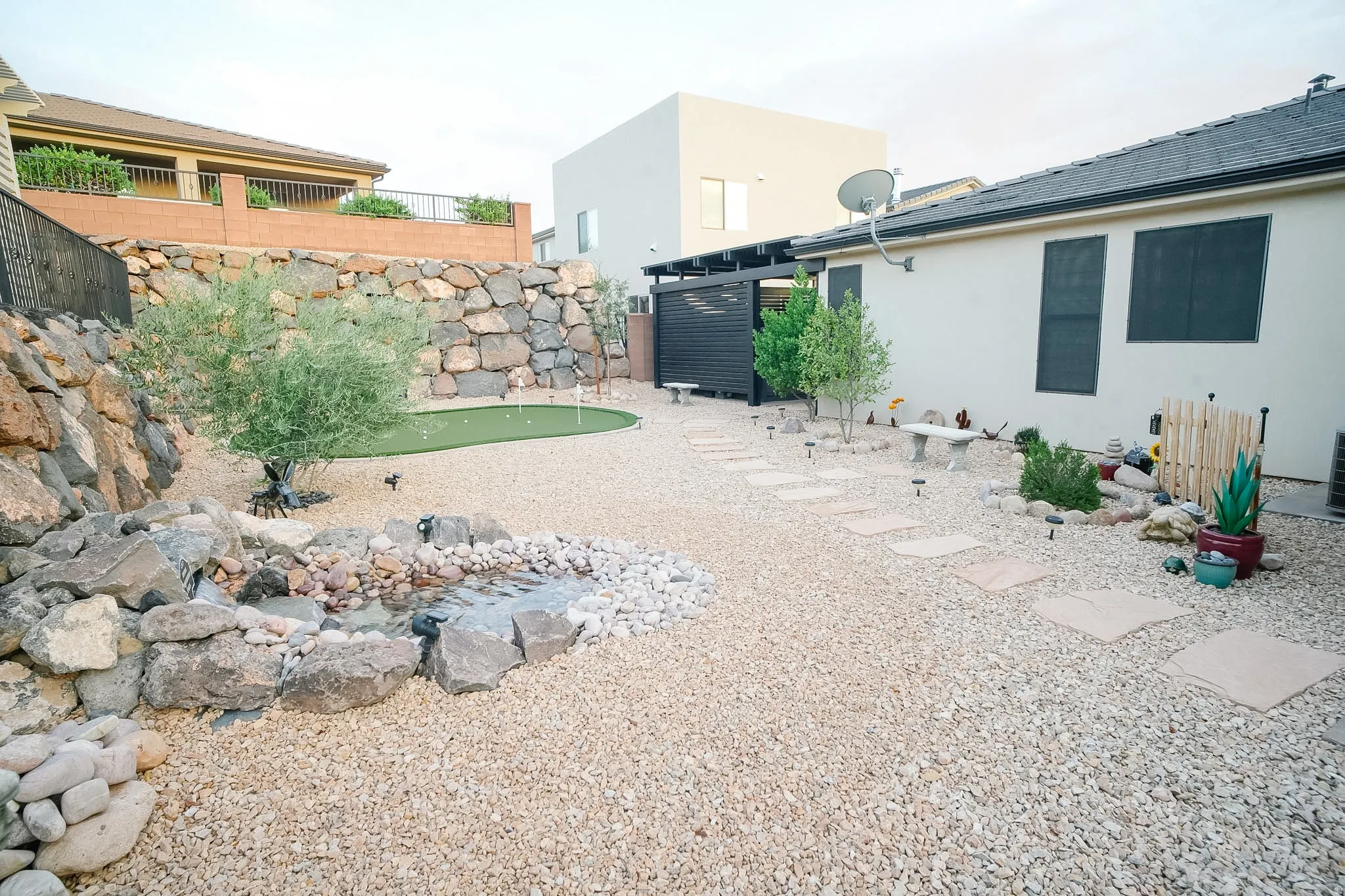 Expansive outdoor space featuring a putting green, a rock-lined water feature, and a gravel-covered surface