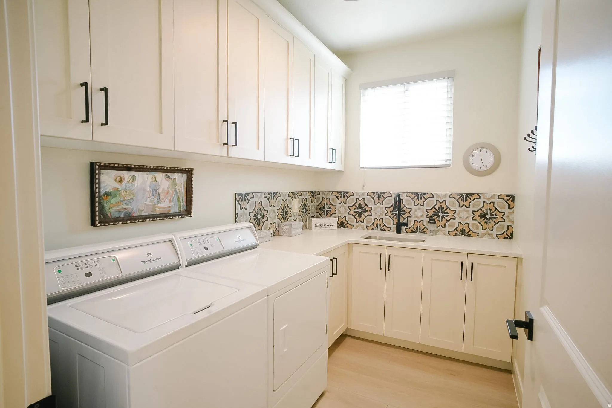 Laundry room featuring extensive white cabinetry with matte black hardware, a built-in sink, and a decorative tile backsplash