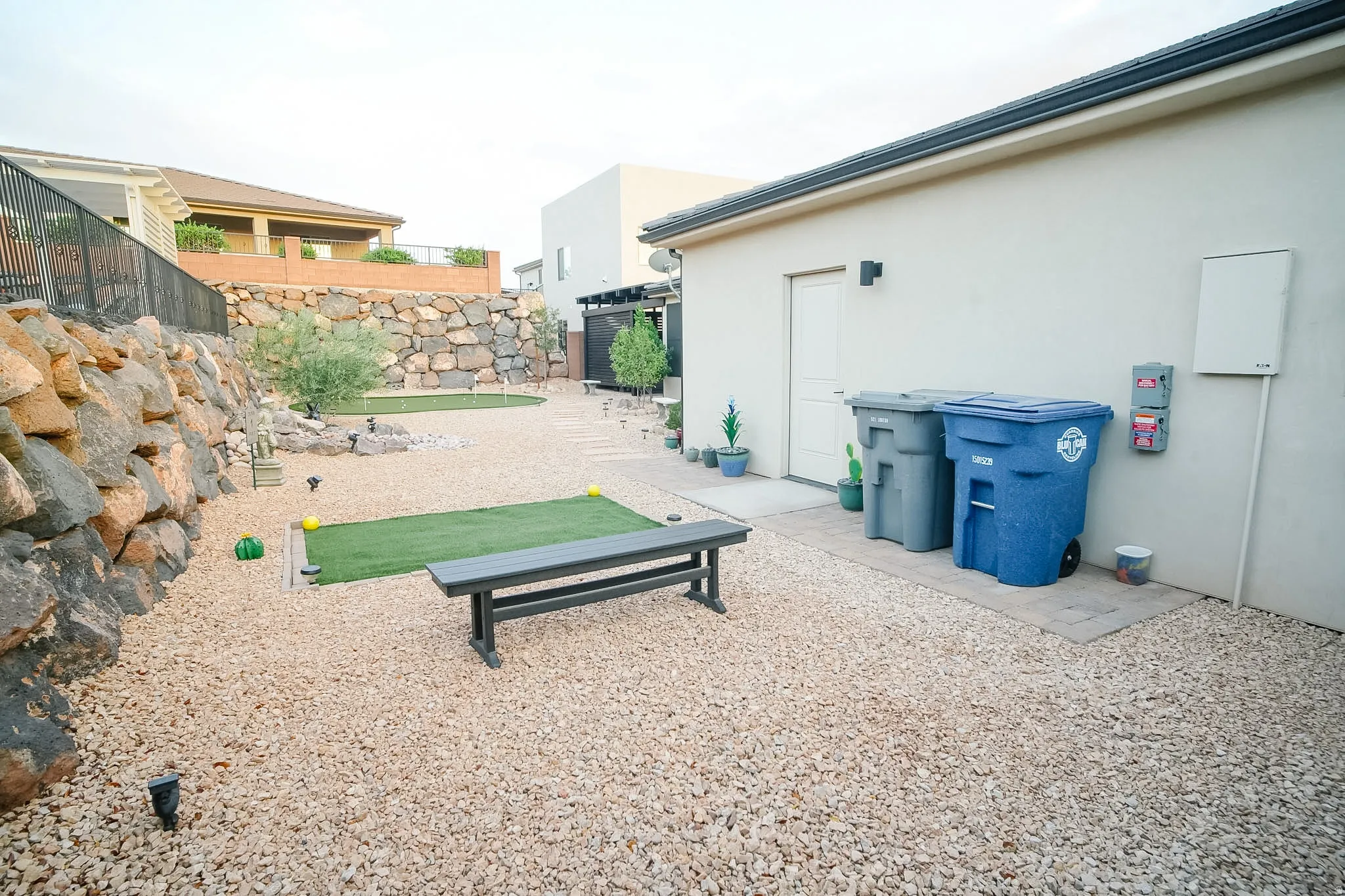 Xeriscaped rear yard featuring extensive light-toned gravel, a rock retaining wall, and a dedicated artificial turf area