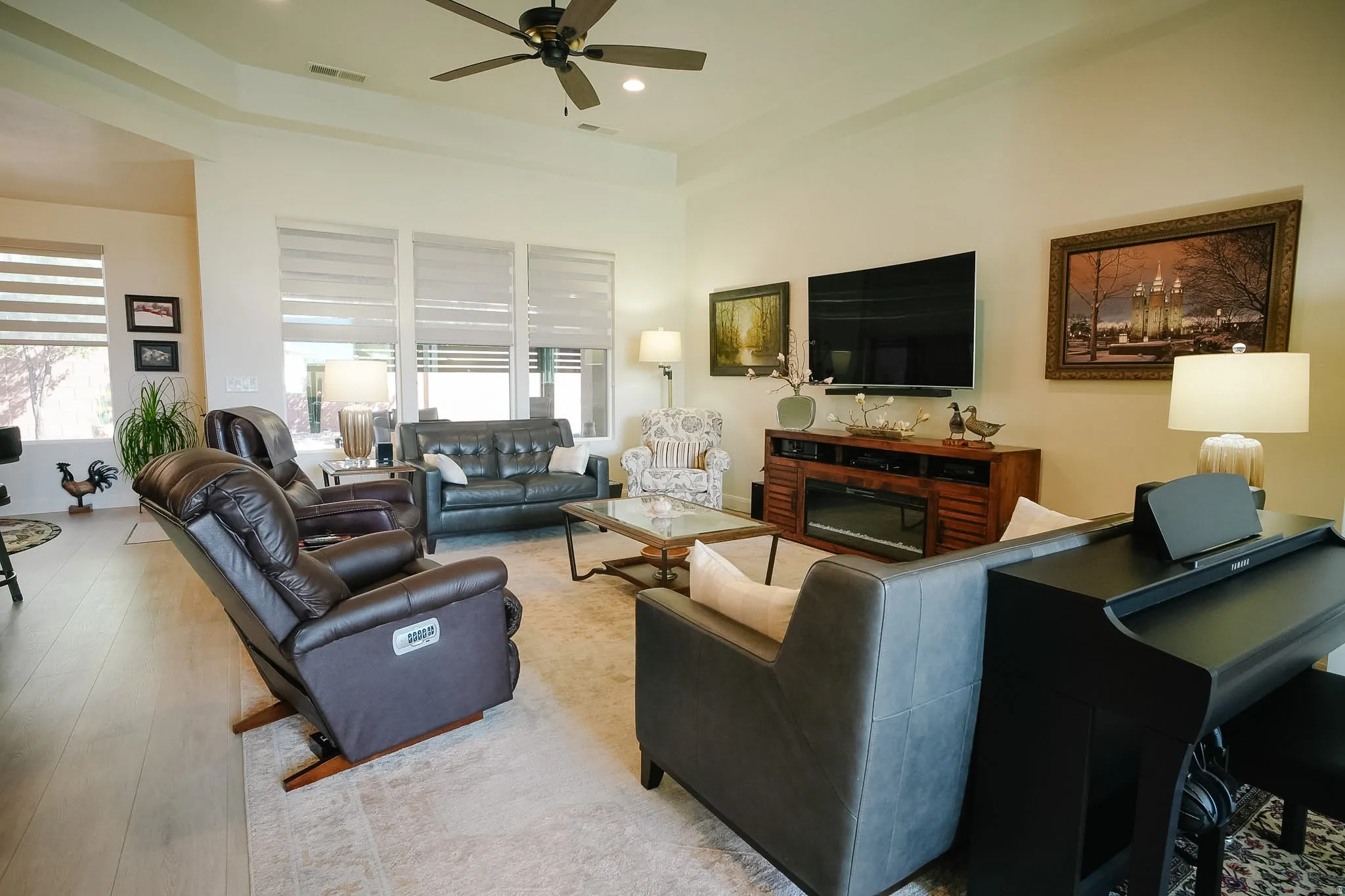 Spacious living area featuring wood-finish flooring, a tray ceiling with a ceiling fan, and large windows with blinds