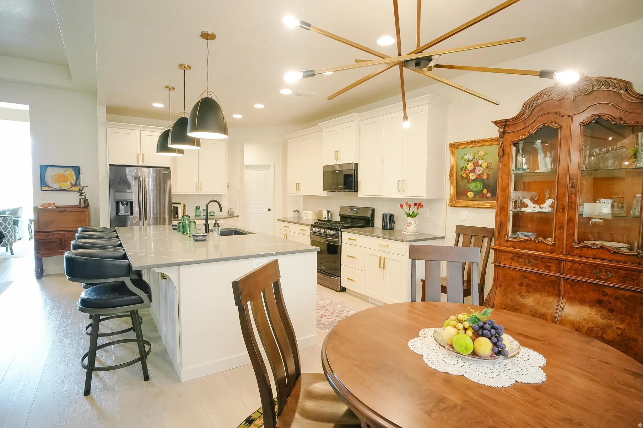 Spacious kitchen featuring an expansive island with undermount sink, white cabinetry with gold-tone hardware, and light wood-finish flooring