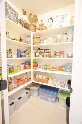 Corner pantry featuring L-shaped shelving, white wood-finish shelving, and light wood-finish flooring