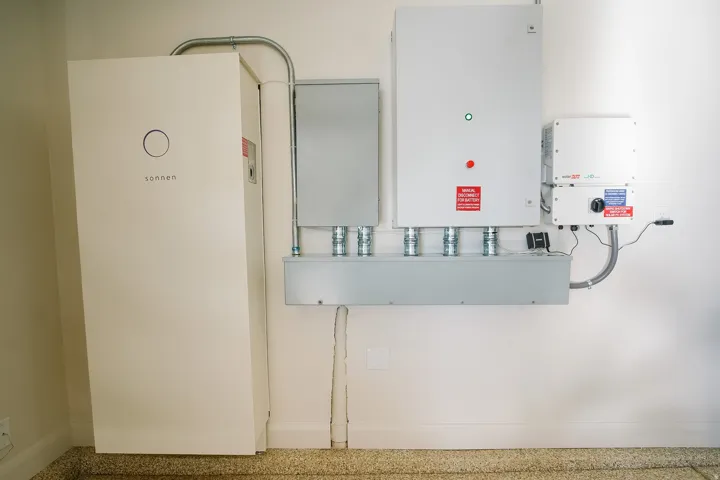 Installed solar energy system components featuring multiple control panels and a large battery storage unit