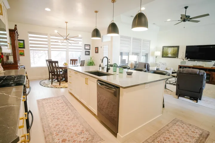 Open-concept living area featuring a kitchen island with stone countertops and a built-in sink, light wood-finish flooring, and recessed lighting