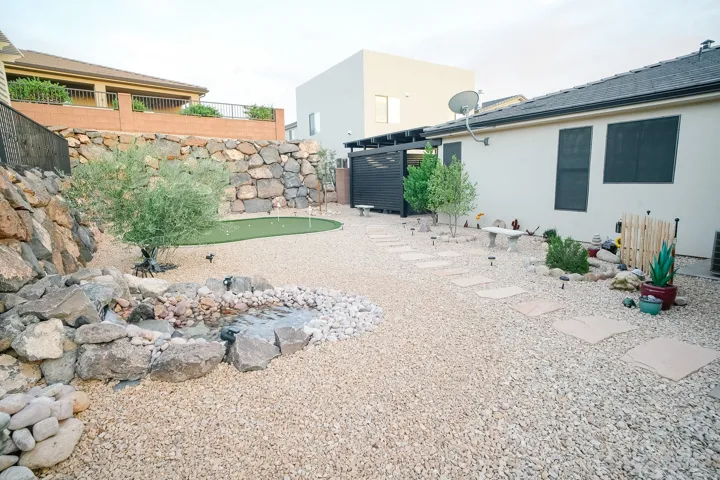 Expansive outdoor space featuring a putting green, a rock-lined water feature, and a gravel-covered surface