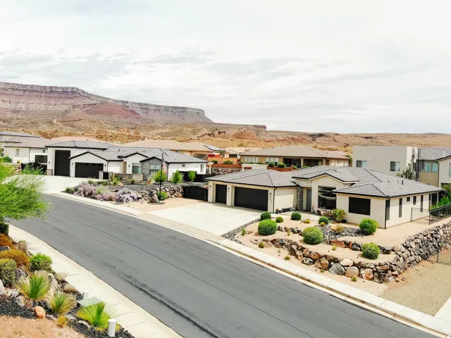 Modern exterior with a light stucco finish, a dark tile roof, a two-car garage, and desert-adapted landscaping