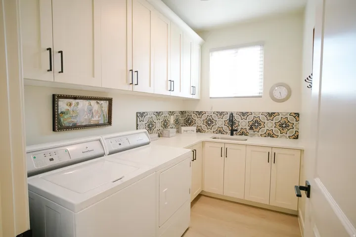 Laundry room featuring extensive white cabinetry with matte black hardware, a built-in sink, and a decorative tile backsplash