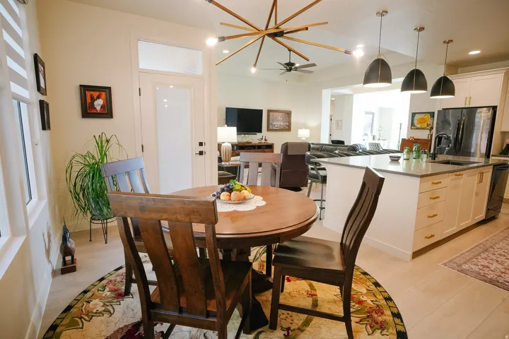 Open-concept living space featuring a modern kitchen island with pendant lighting, light-toned wood-finish flooring, and white cabinetry with gold-tone hardware