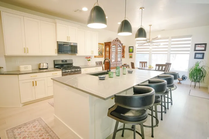 Spacious kitchen featuring an expansive center island with seating, light-toned cabinetry, light wood-finish flooring, a stainless steel range with a microwave, and ample natural light from large windows