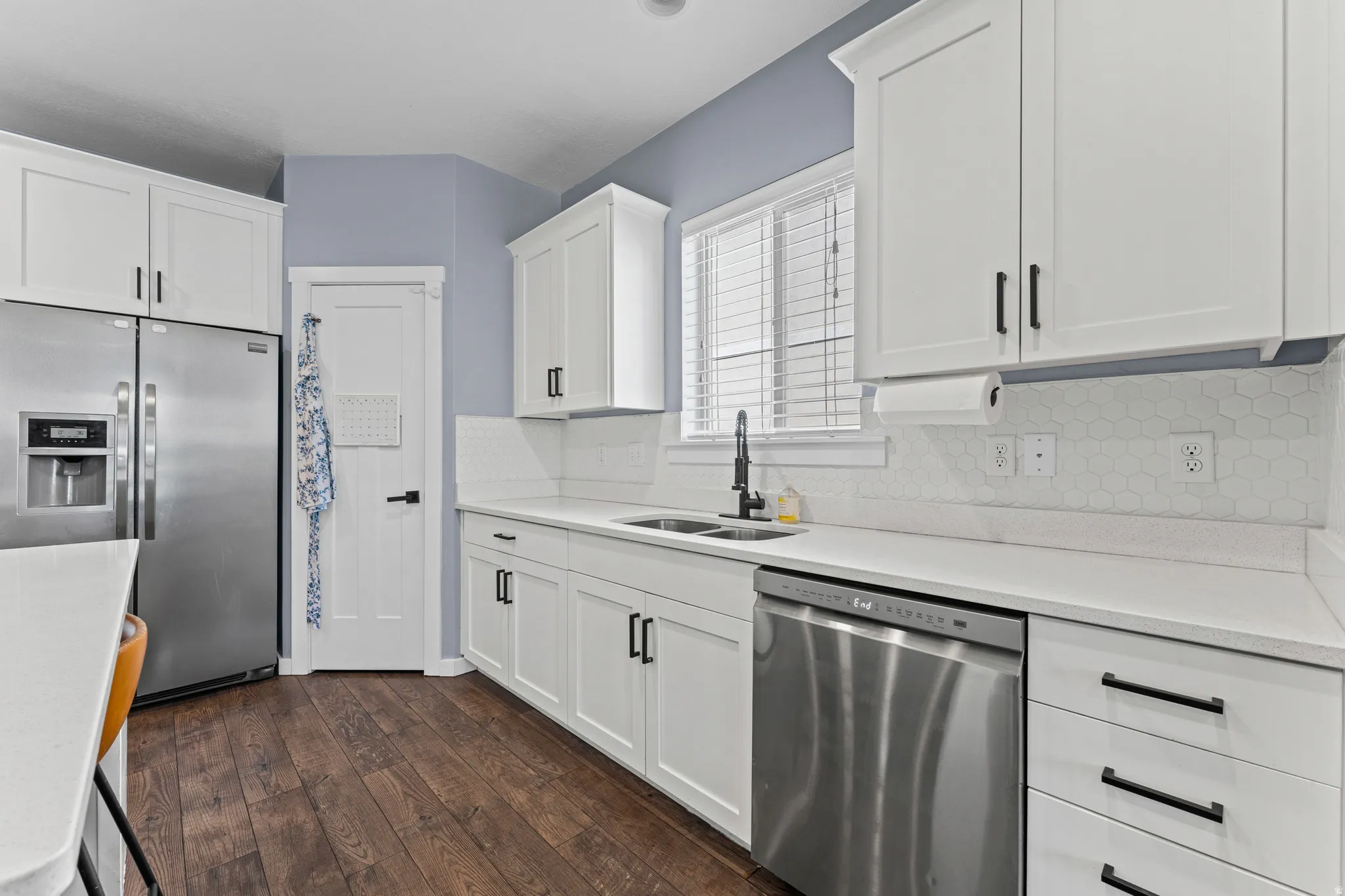 Modern kitchen featuring white shaker cabinetry, stainless steel appliances, a hexagon tile backsplash, and dark wood-finish flooring