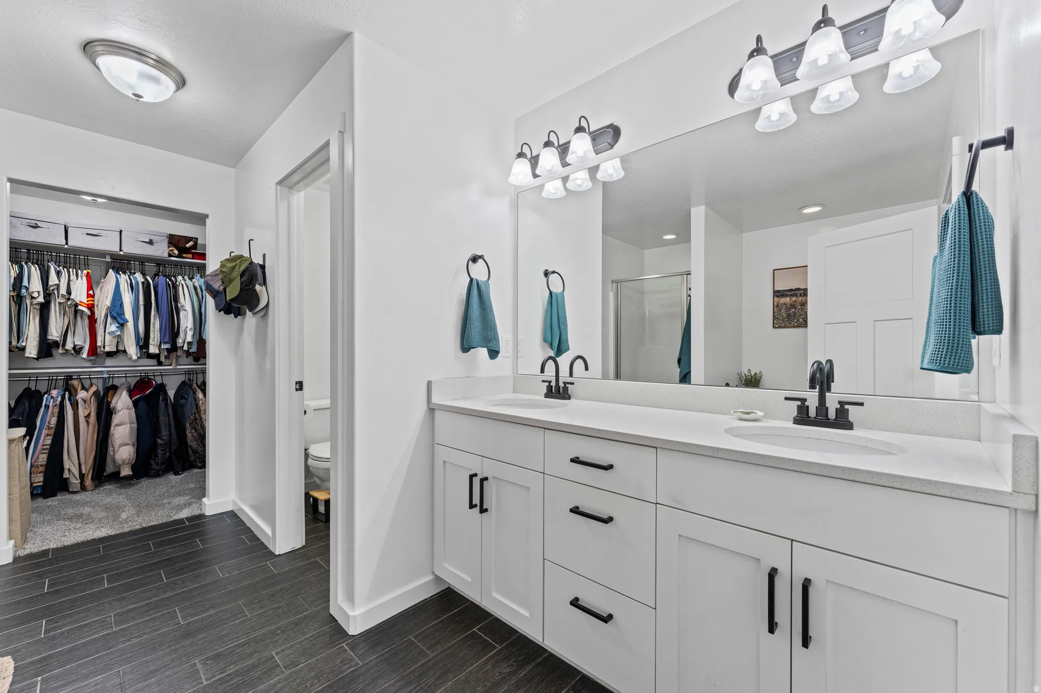 Bathroom featuring a dual vanity with white cabinetry and dark hardware, set against a full-width mirror with a six-light fixture