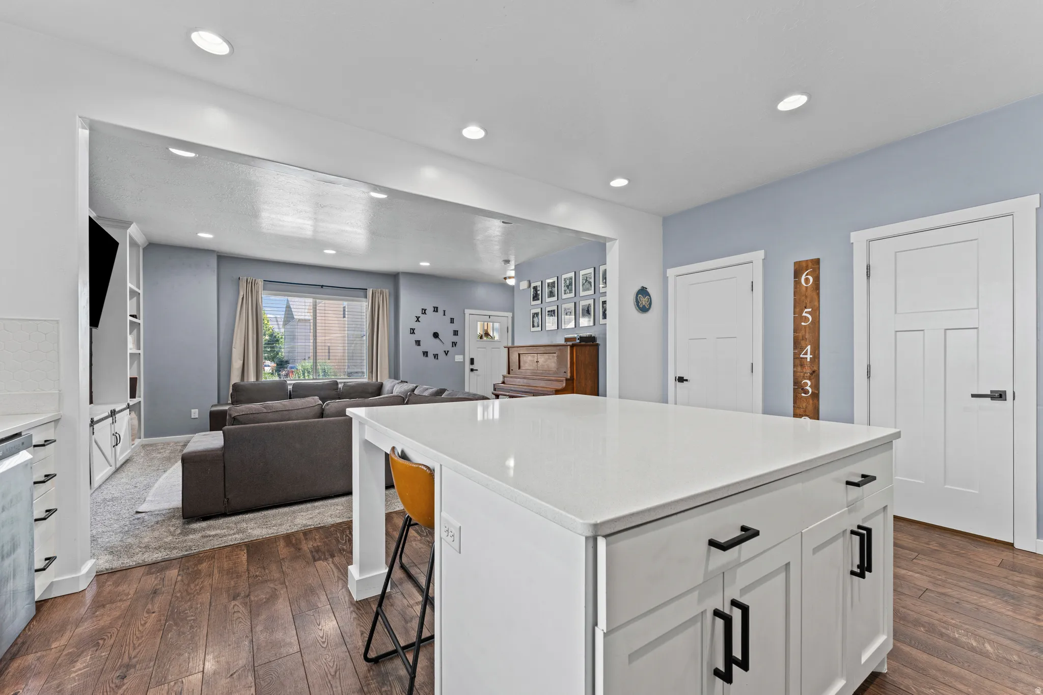 Spacious kitchen island with a white countertop and contrasting dark hardware, hardwood-finish flooring, recessed lighting, and white paneled doors