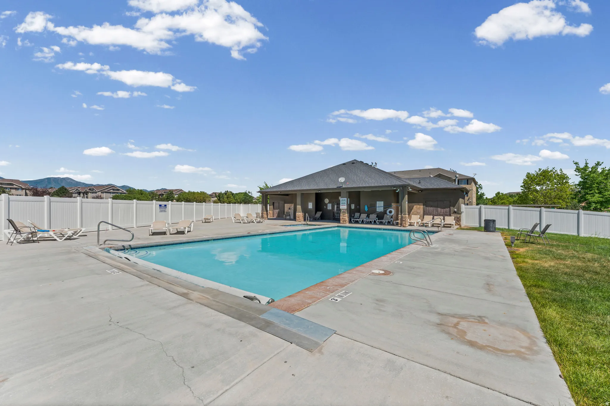 Community swimming pool with a concrete deck, white perimeter fencing, and a nearby covered amenity building