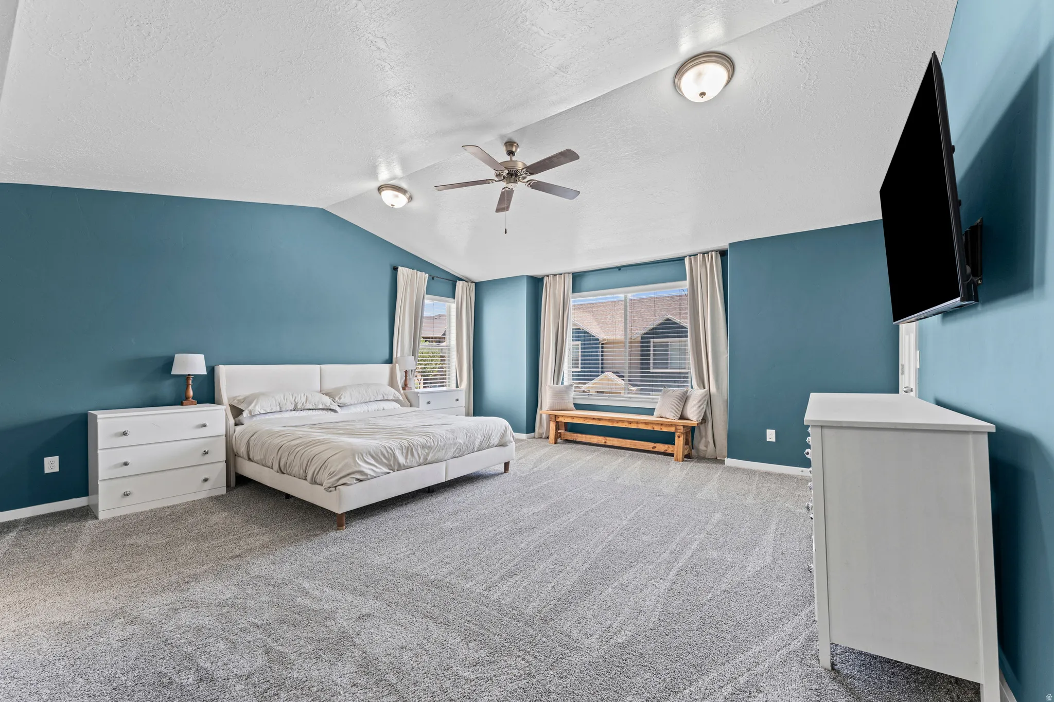 Spacious room featuring vaulted ceilings, plush carpeting, and deep teal accent walls