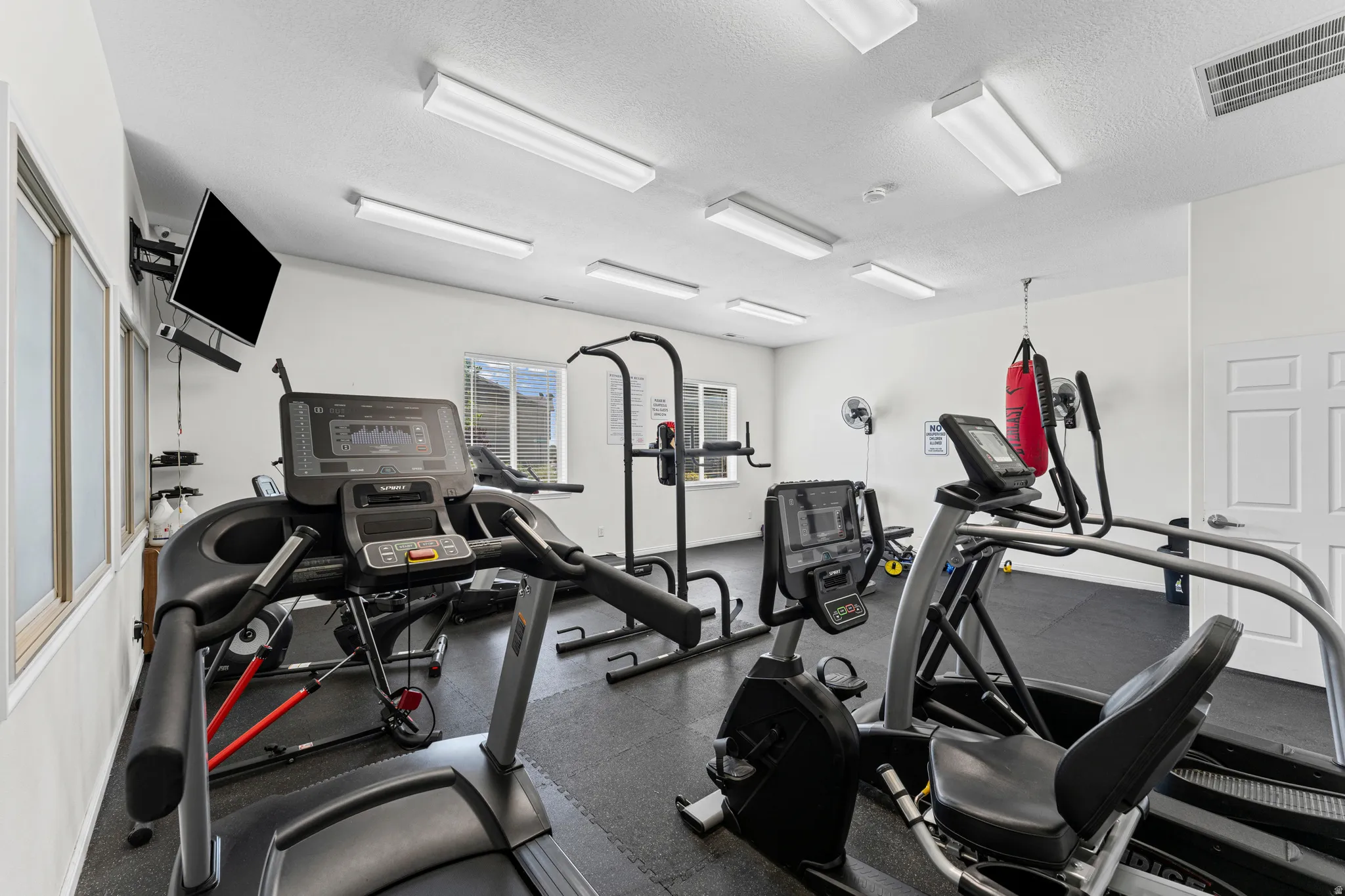 Dedicated fitness room featuring recessed lighting, a mounted television, dual windows with natural light, and durable rubber flooring