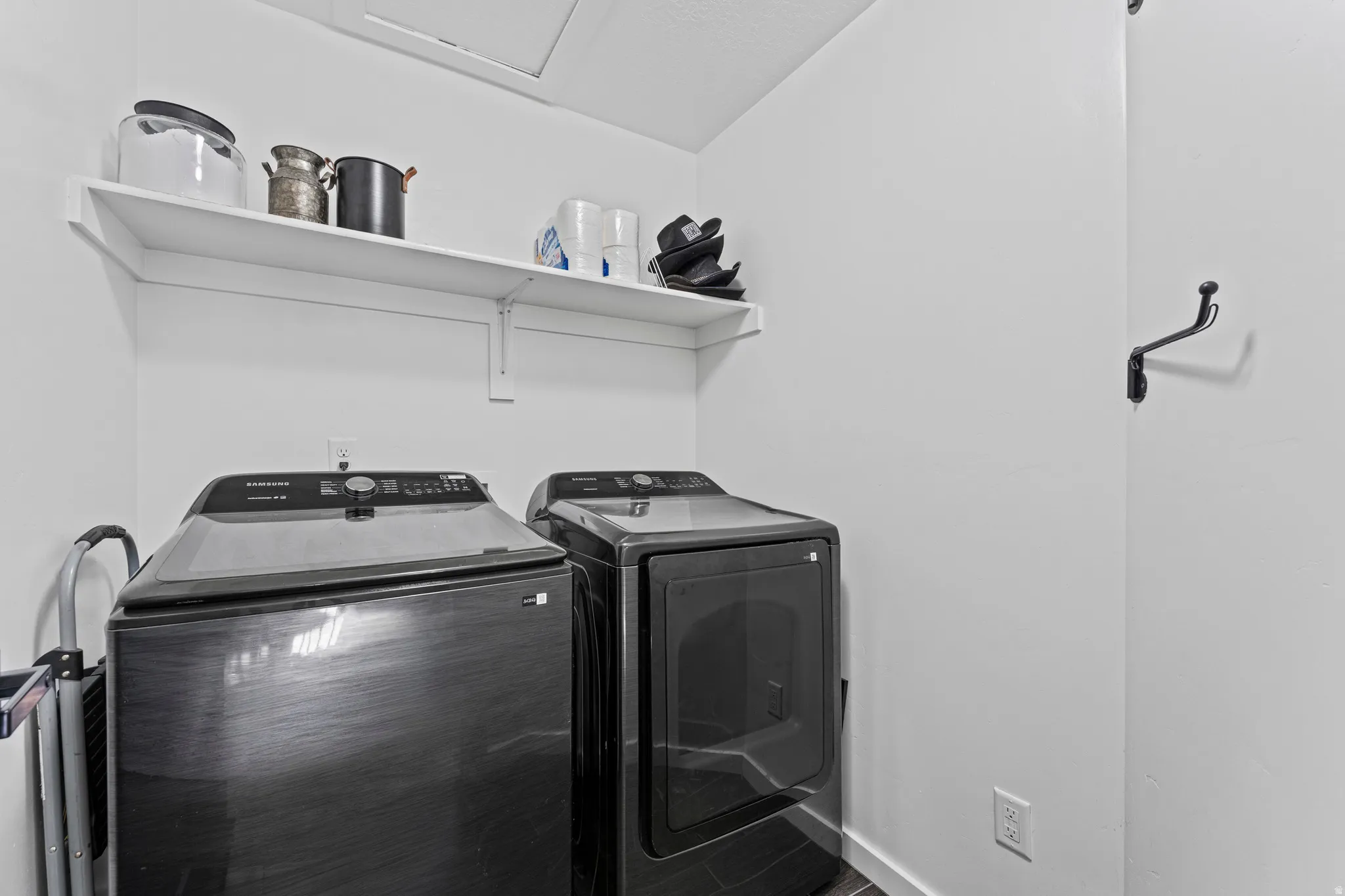 Dedicated laundry area featuring a wall-mounted shelf, dark-toned appliances, and a wall-mounted coat rack