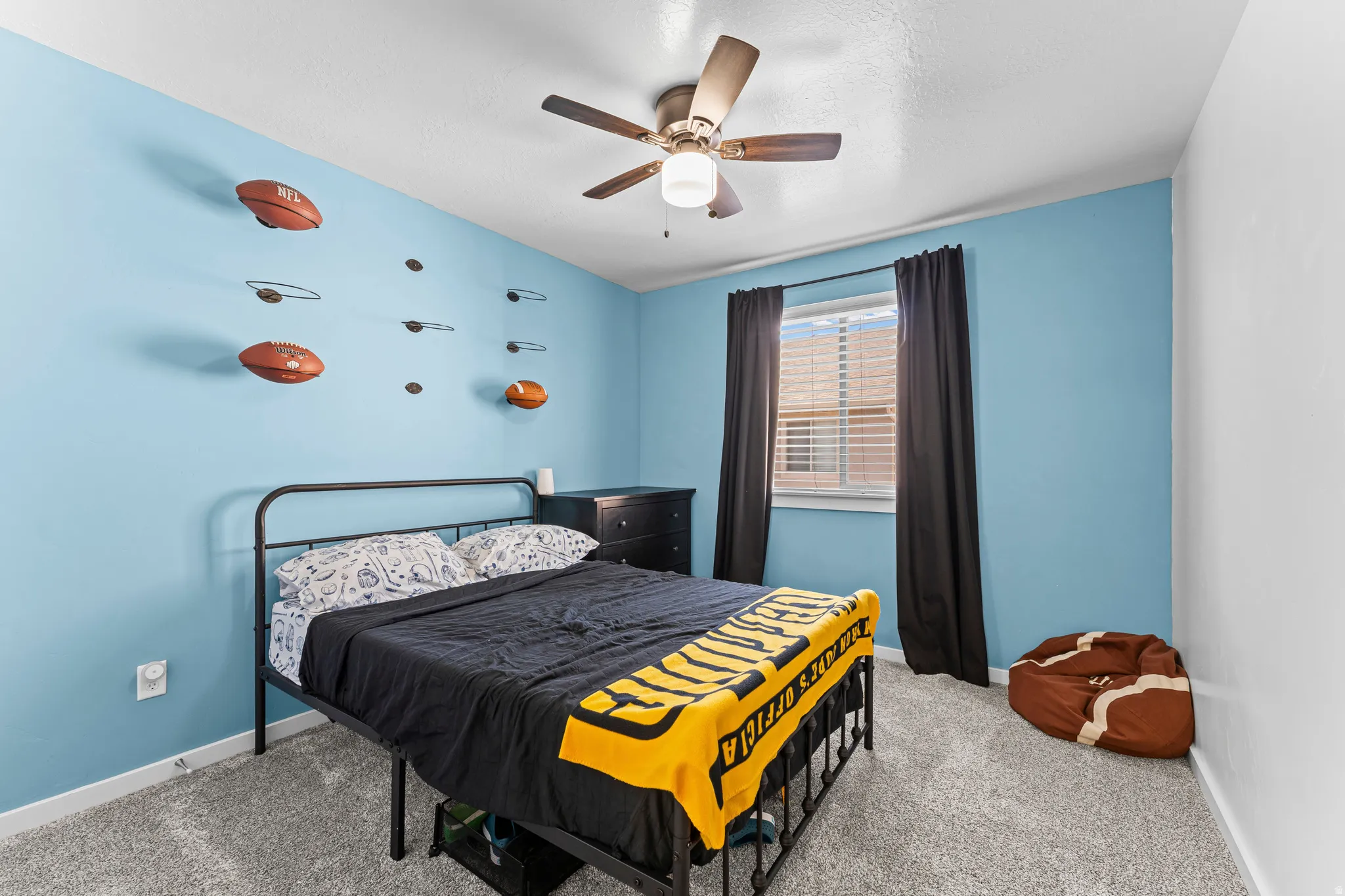 Bedroom featuring light blue walls, gray carpet, a ceiling fan with light fixture, and a window with blinds and dark curtains