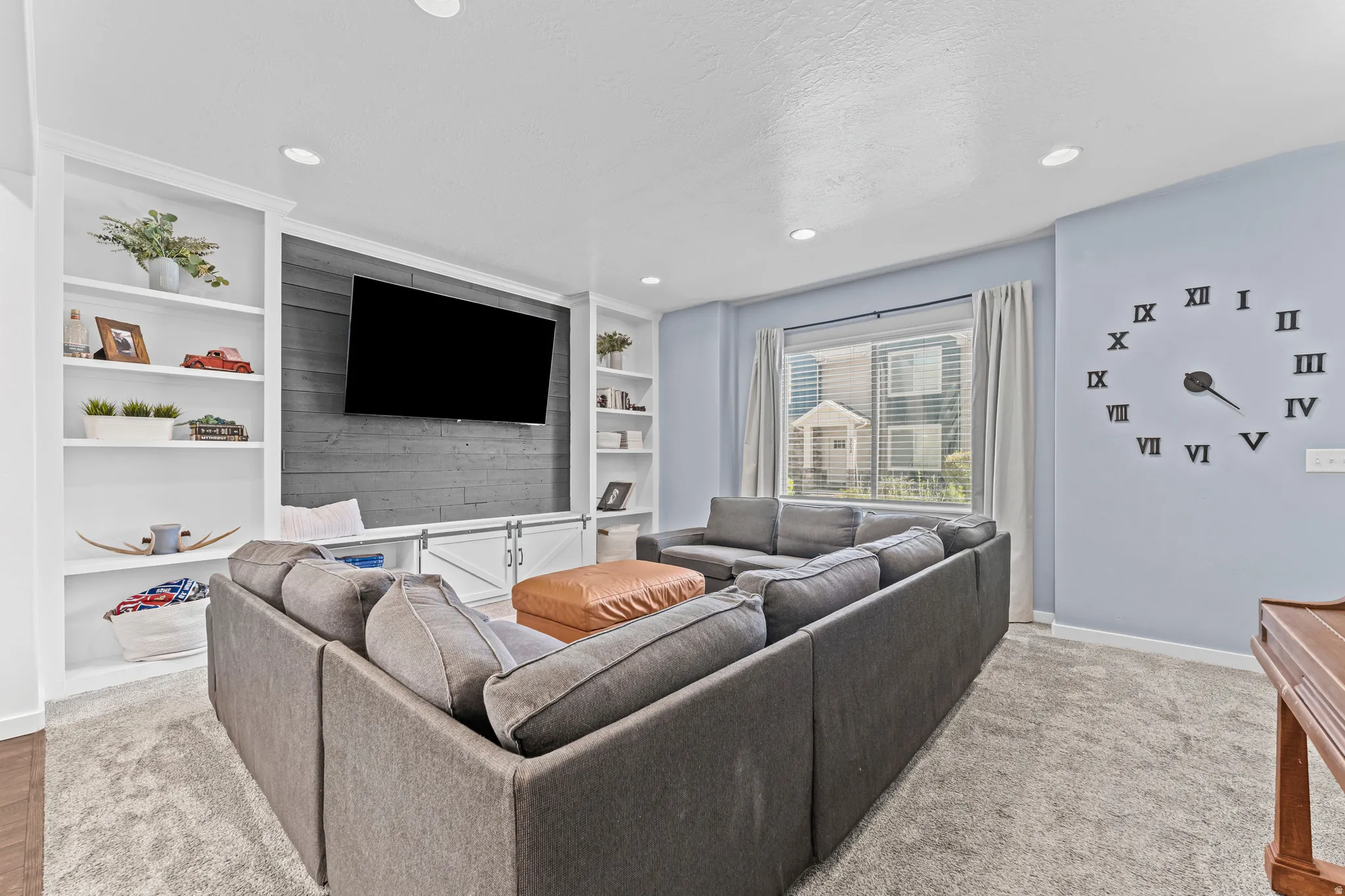 Spacious living area featuring a built-in entertainment center with open shelving, shiplap accent wall, and integrated storage with barn door accents