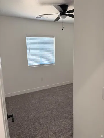 Carpeted room featuring a ceiling fan with light fixture, window with blinds, and white baseboards