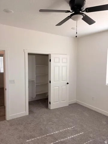 Bedroom featuring plush gray carpeting, white walls, and a black ceiling fan with integrated lighting