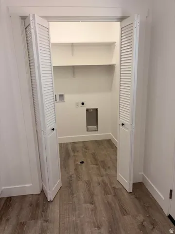 Dedicated laundry area featuring wood-finish flooring, white louvered bi-fold doors, and built-in shelving