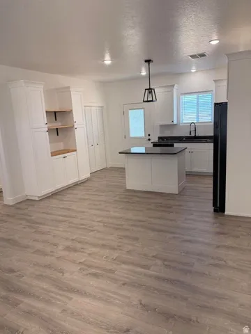Open-concept kitchen featuring white cabinetry, a central island with a dark countertop, and wood-finish flooring