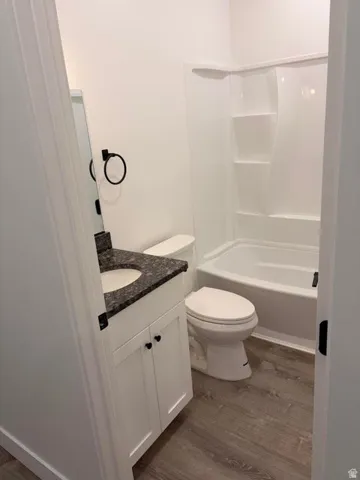 Bathroom featuring a white vanity with dark countertop, an undermount sink, a white toilet, and a white tub/shower combination with integrated shelving