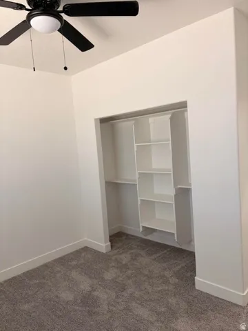 Recessed closet with built-in shelving, gray textured carpet, white baseboards, and a black ceiling fan with an integrated light fixture