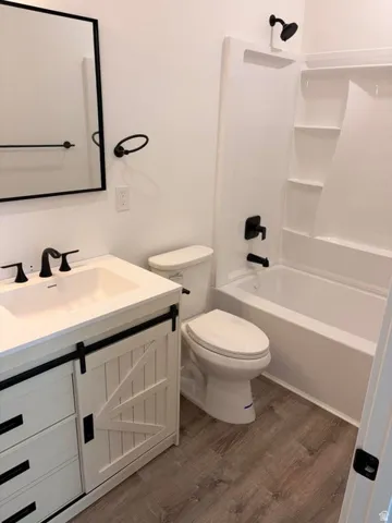 Bathroom featuring a white vanity with barn door style cabinetry, a white basin sink, matte black hardware, and wood-finish flooring