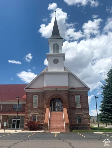 Stone facade building with a prominent steeple, featuring a sloped red roof and multiple windows
