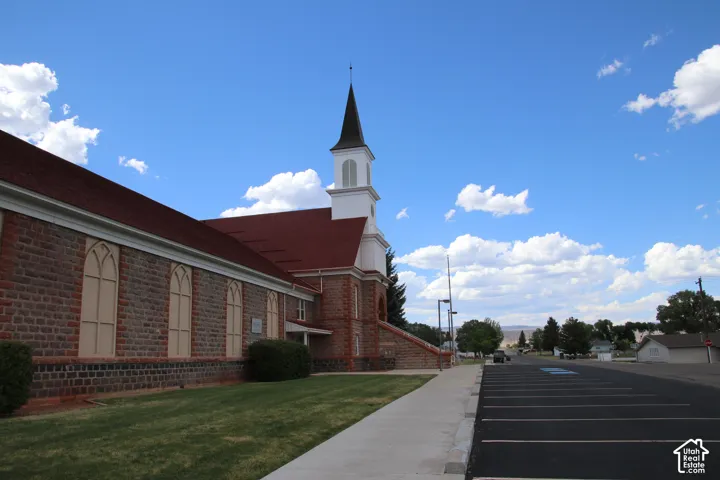 Stone-clad building with a prominent steeple, arched window details, a red shingle roof, and an expansive asphalt parking lot