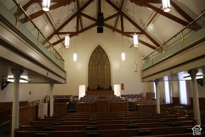 Grand interior featuring a vaulted ceiling with exposed wood beams, a large arched window, and suspended pendant lighting