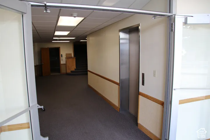 Stainless steel elevator with a paneled ceiling, carpet flooring, wood wainscoting, and recessed lighting