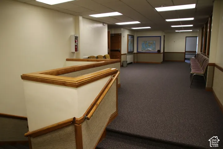 Carpeted hallway featuring wood-finish handrails and trim