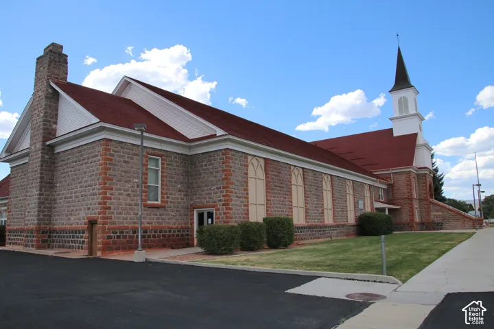 Stone facade building featuring a prominent steeple, a red shingle roof, and arched window details