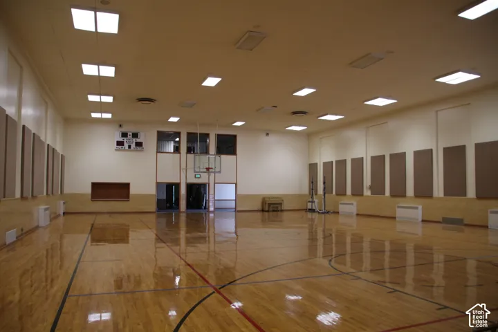 Spacious indoor court featuring polished wood flooring with court markings, recessed ceiling lighting, sound-dampening wall panels, a visible scoreboard, and multiple wall-mounted heating units