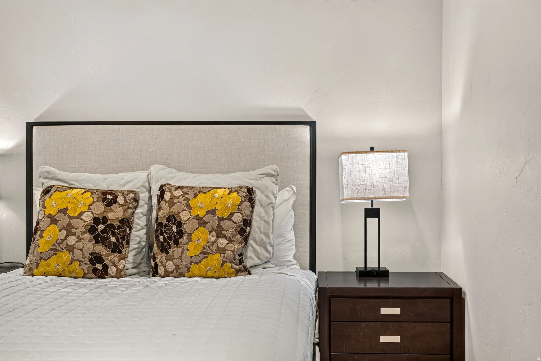 Upholstered headboard with a dark frame, flanked by a dark wood nightstand featuring two drawers with linear silver hardware