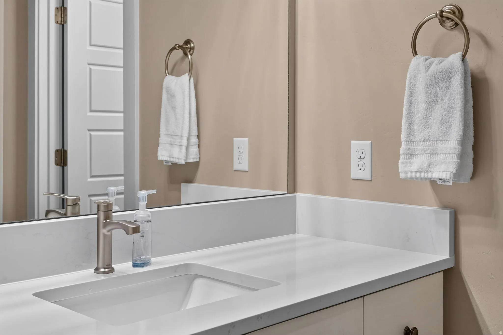 Bathroom vanity featuring an integrated rectangular sink, brushed nickel faucet, and white countertop with backsplash