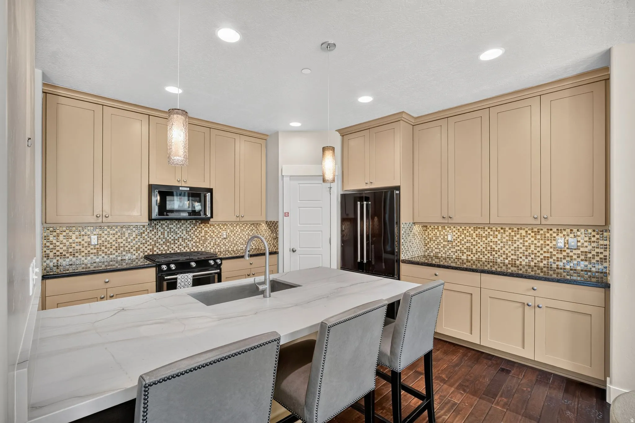 Kitchen featuring a central island with a built-in sink, stone countertop, and two pendant lights