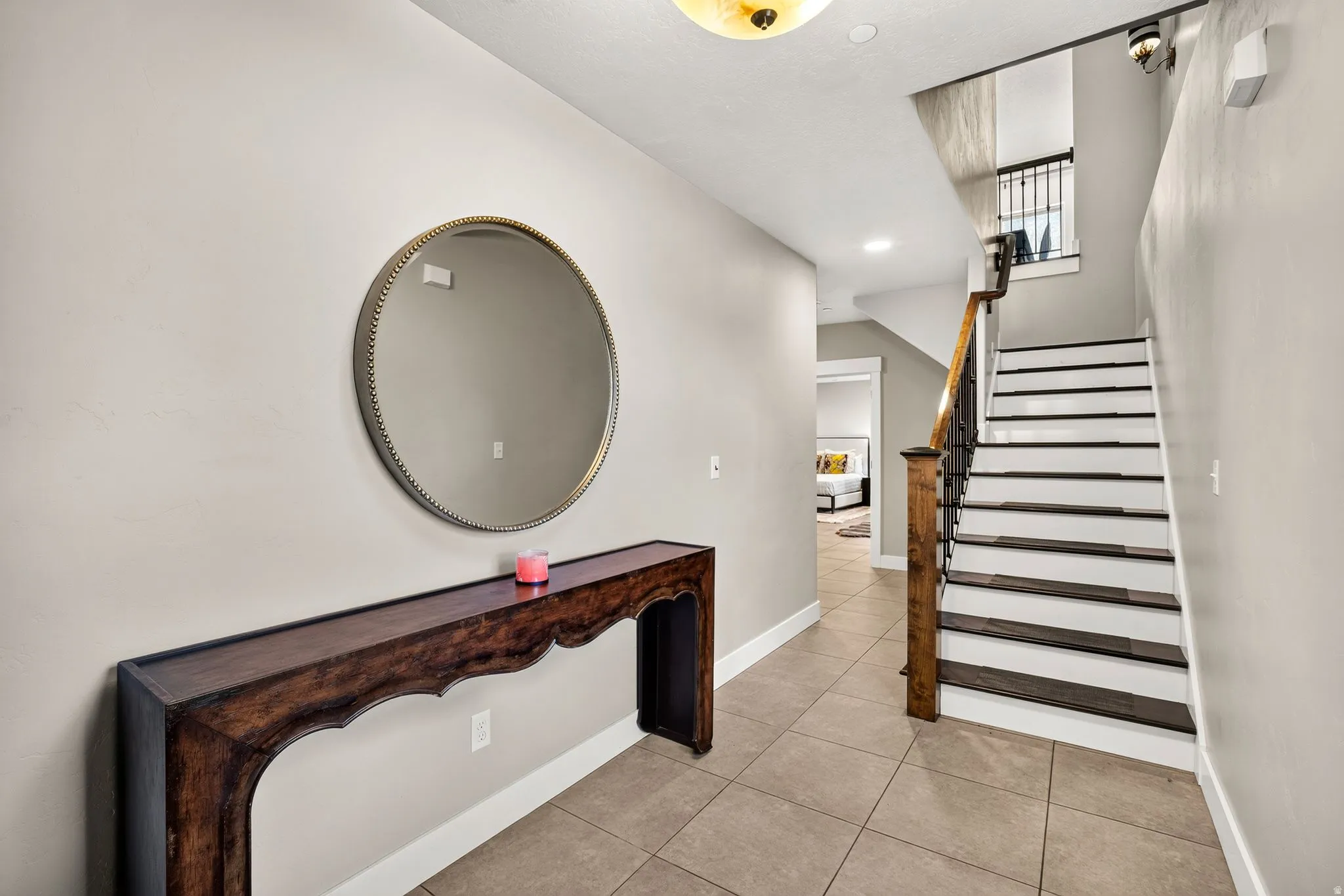 Tiled entryway featuring a staircase with painted risers and dark wood-finish treads, a wood newel post, and wrought iron balusters