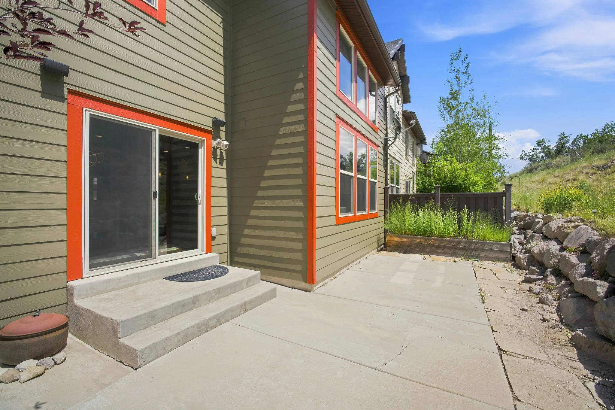 Rear exterior featuring a sliding glass door with contrasting trim, a concrete patio, and a tiered stone retaining wall