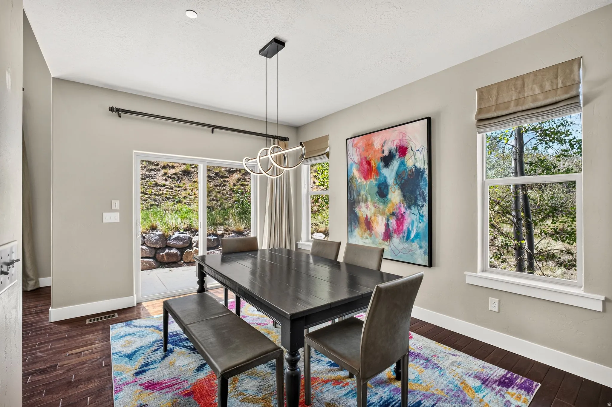 Dining area with dark wood-finish flooring, light-toned walls, and a contemporary chandelier