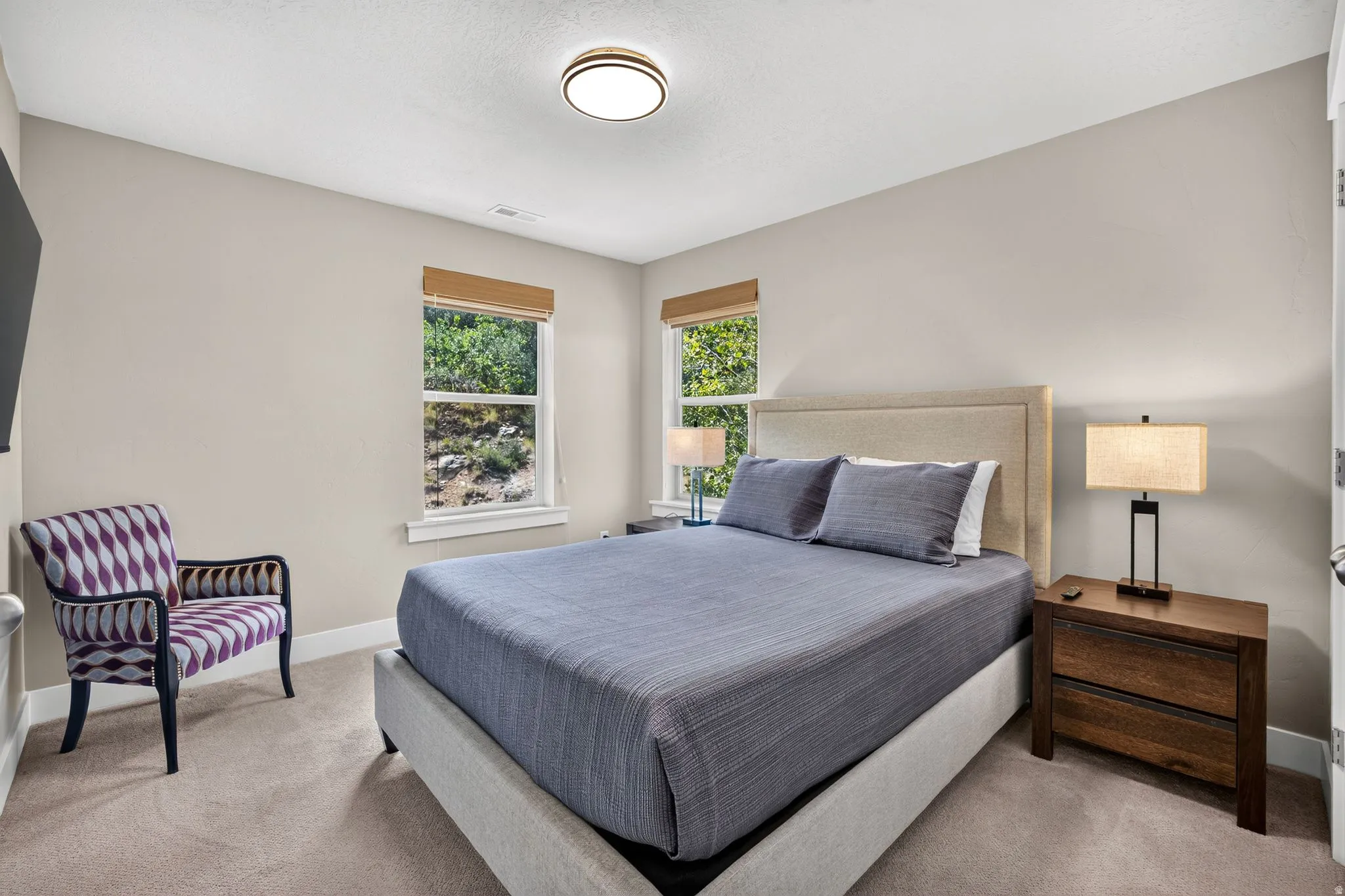 Bedroom featuring plush carpet flooring, neutral paint palette, two windows with natural wood blinds, and a flush mount ceiling light fixture