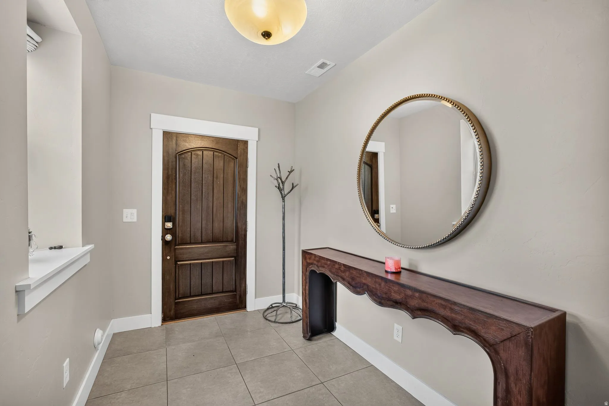 Entryway featuring a paneled wood door with white trim, a decorative round mirror, and tile flooring